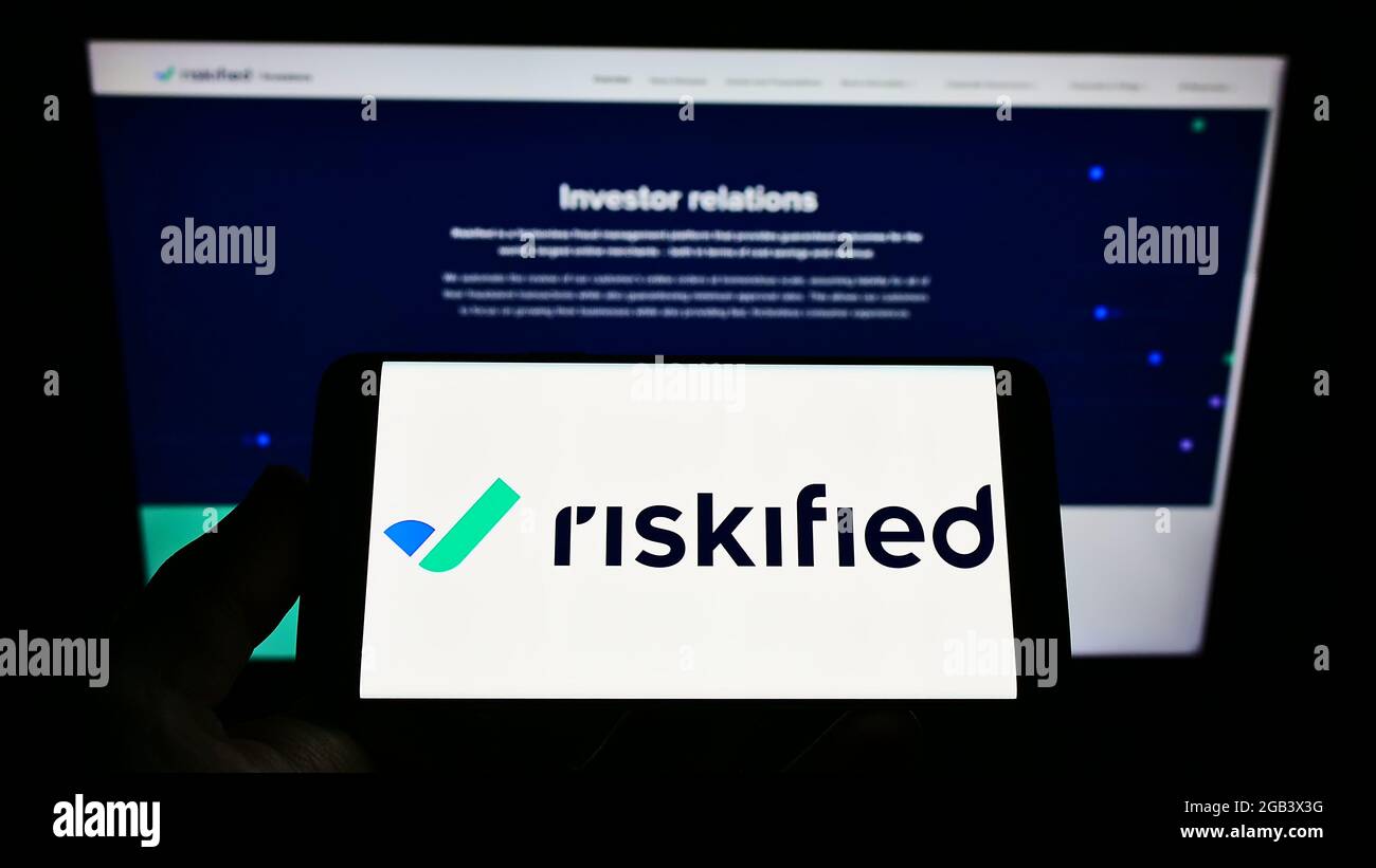 Person holding cellpohone with logo of fraud prevention software company Riskified Ltd. on screen in front of webpage. Focus on phone display. Stock Photo