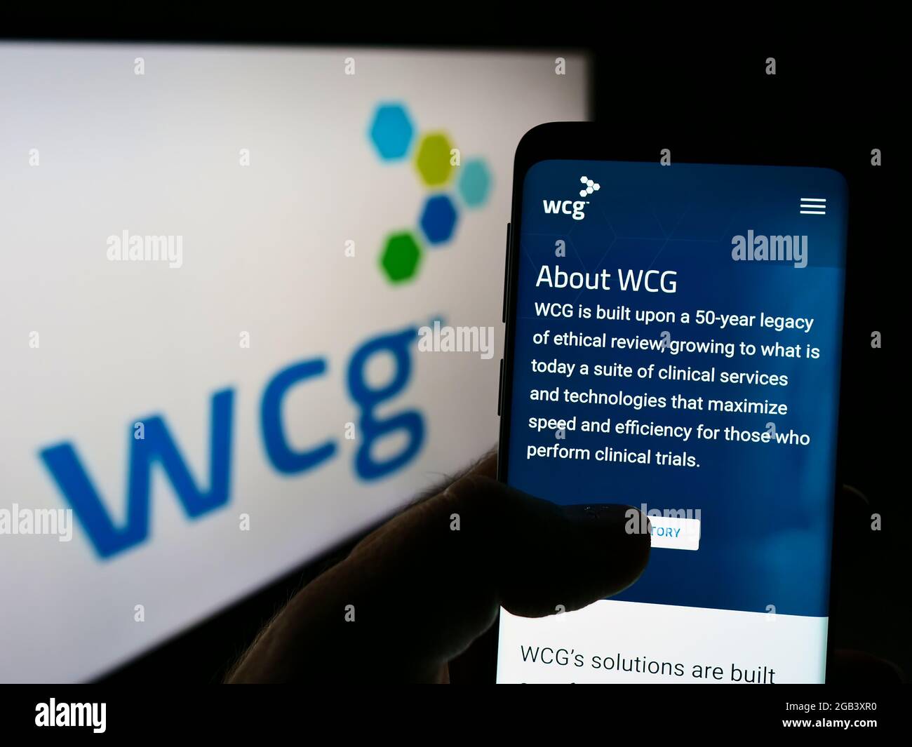 Person holding cellphone with webpage of company WIRB-Copernicus Group Inc. (WCG Clinical) on screen with logo. Focus on center of phone display. Stock Photo