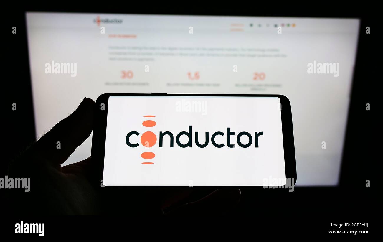 Person holding cellphone with logo of Brazilian payment company Conductor Technology Ltd. on screen in front of webpage. Focus on phone display. Stock Photo