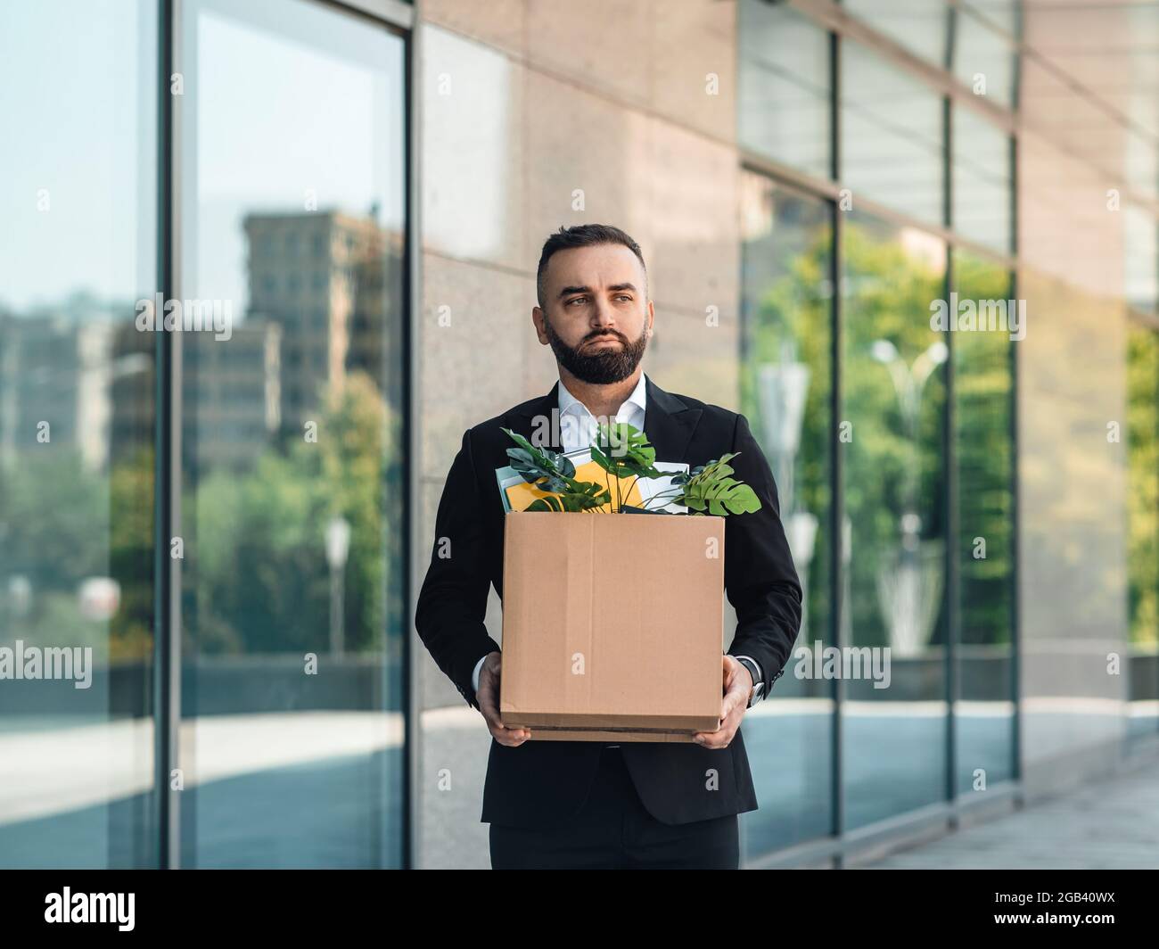 Man is upset by dismissal, lost his job. Fired male worker moving out office with box full of belongings, copy space Stock Photo