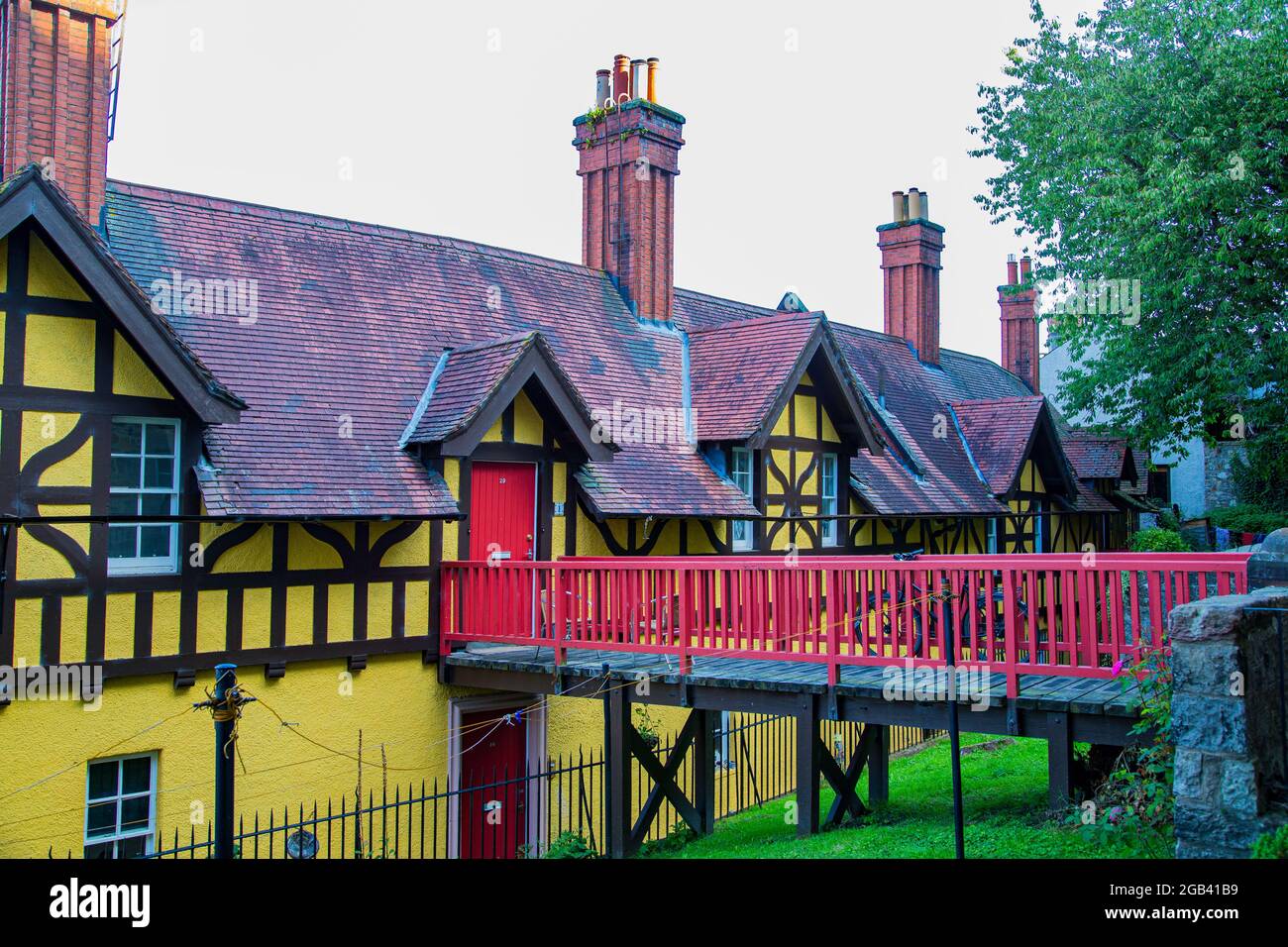 Wooden walkway with red railings, to house with yellow facade and gabled roof Stock Photo