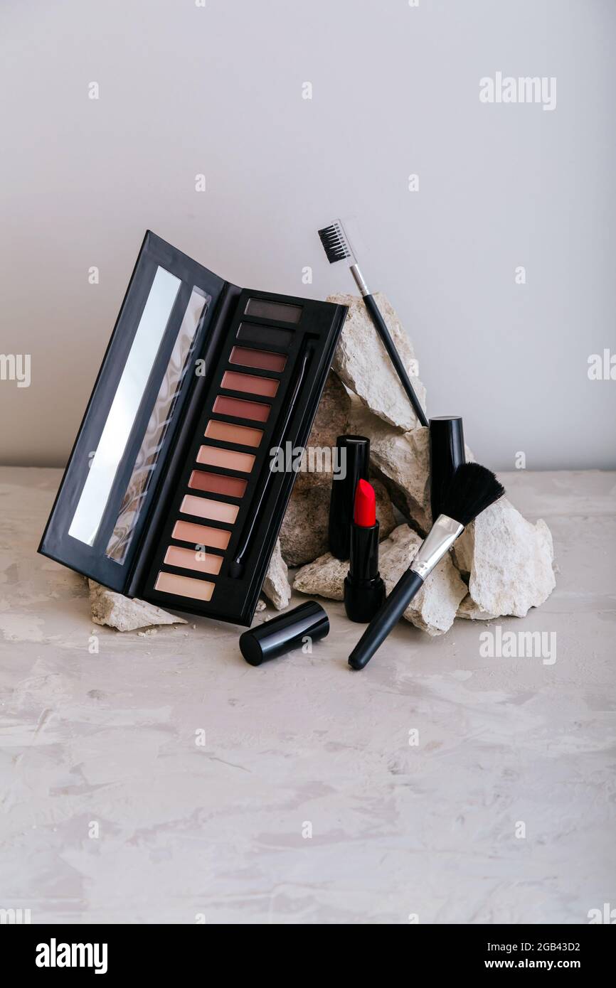 Decorative cosmetics for makeup on stone pedestal. Red scarlet lipstick eyeshadow makeup brushes on gray concrete background. Minimal aesthetic Stock Photo