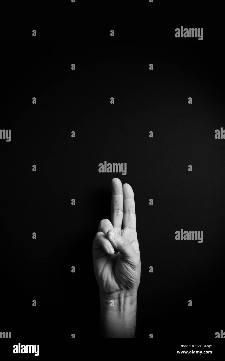 Dramatic B&W image of male hand demonstrating ASL American sign language letter U with empty copy space for editors Stock Photo