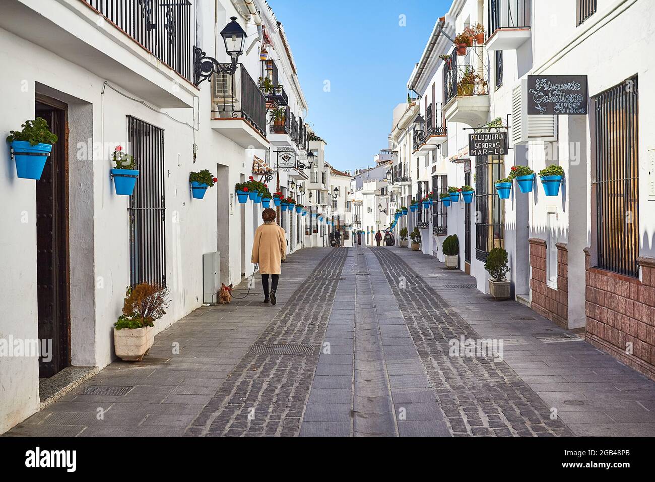 Picturesque street of Mijas with a lady walking a dog. Andalusian white town. Costa del Sol. Southern Spain Stock Photo