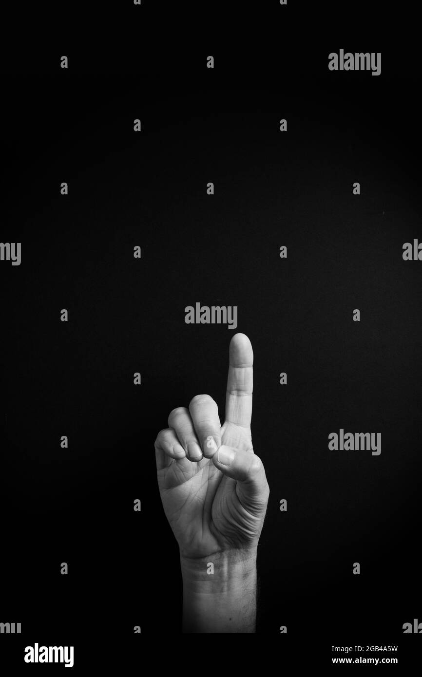 Dramatic B&W image of male hand demonstrating ASL American sign language letter D with empty copy space for editors Stock Photo
