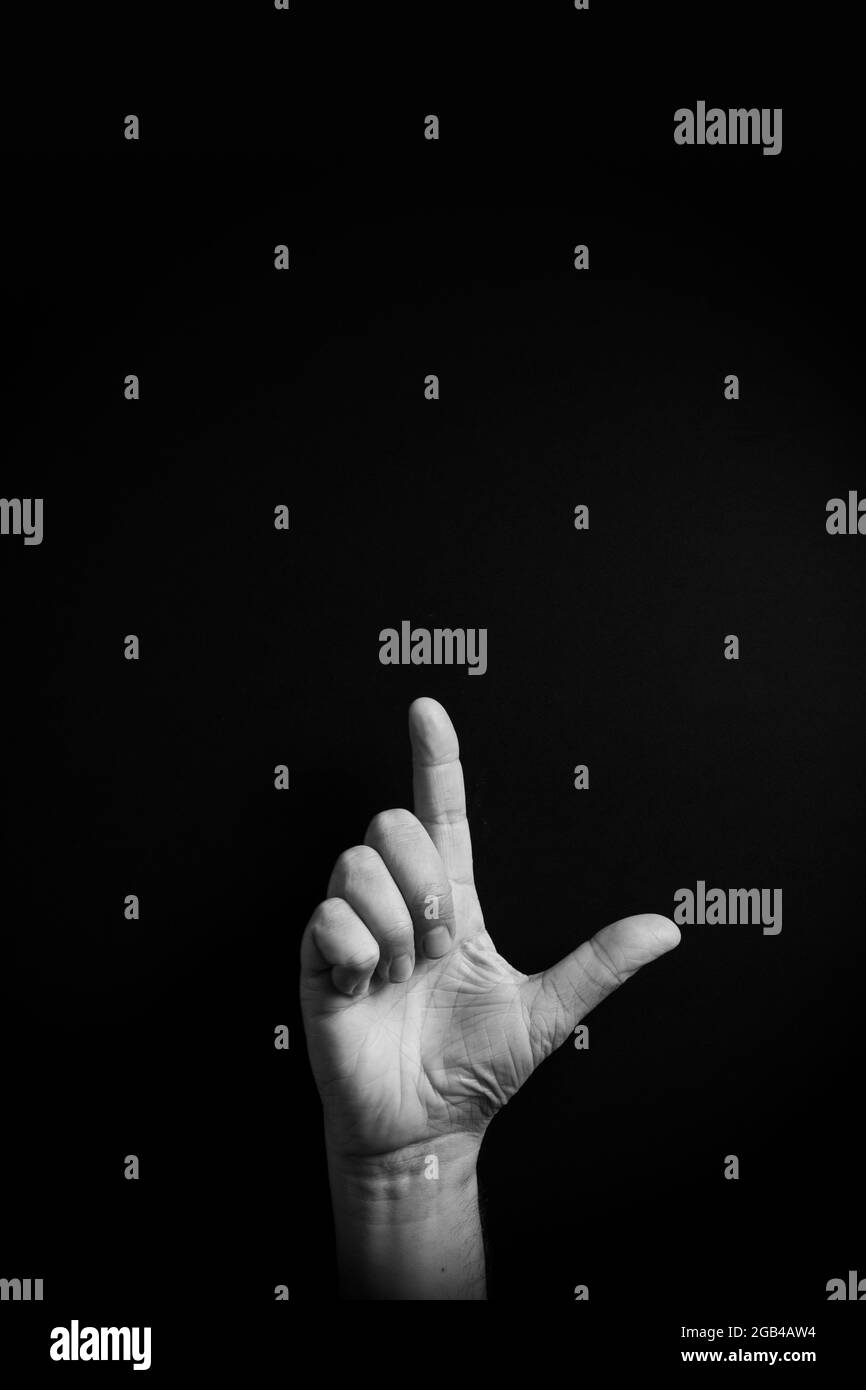 Dramatic B&W image of male hand demonstrating ASL American sign language letter L with empty copy space for editors Stock Photo