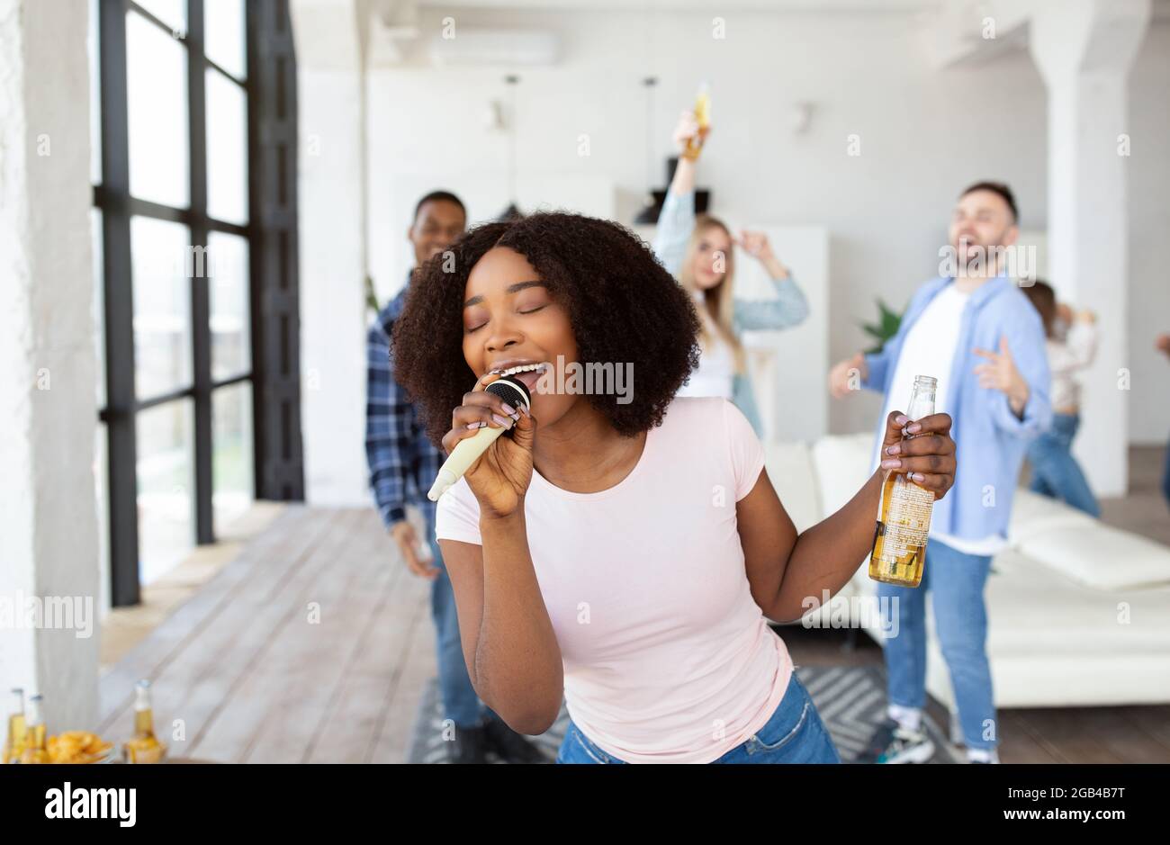 Happy black woman with bottle of beer and microphone performing song