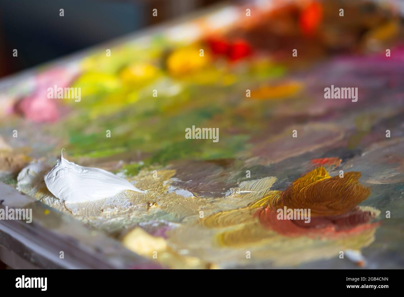 Artist's palette with white oil paint close-up. Blurry multicolored background. Professional paints of the artist in a selective focus. The concept of Stock Photo