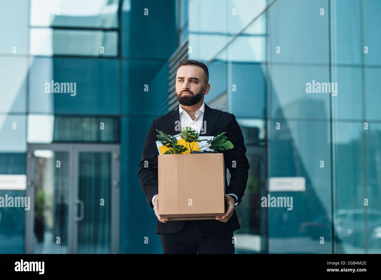 Crisis and unemployment concept. Depressed male office worker holding box and leaving office building, copy space Stock Photo