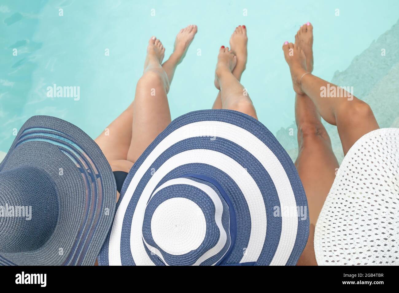 Top view of three women in straw hat relaxing near a swimming pool with ...