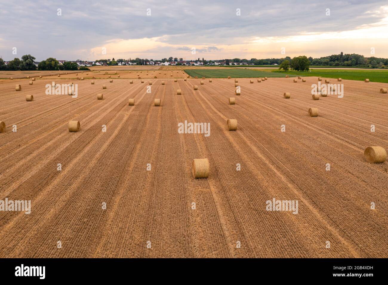 A field with hay bales after the harvest with a view of further fields and a village in backlight Stock Photo