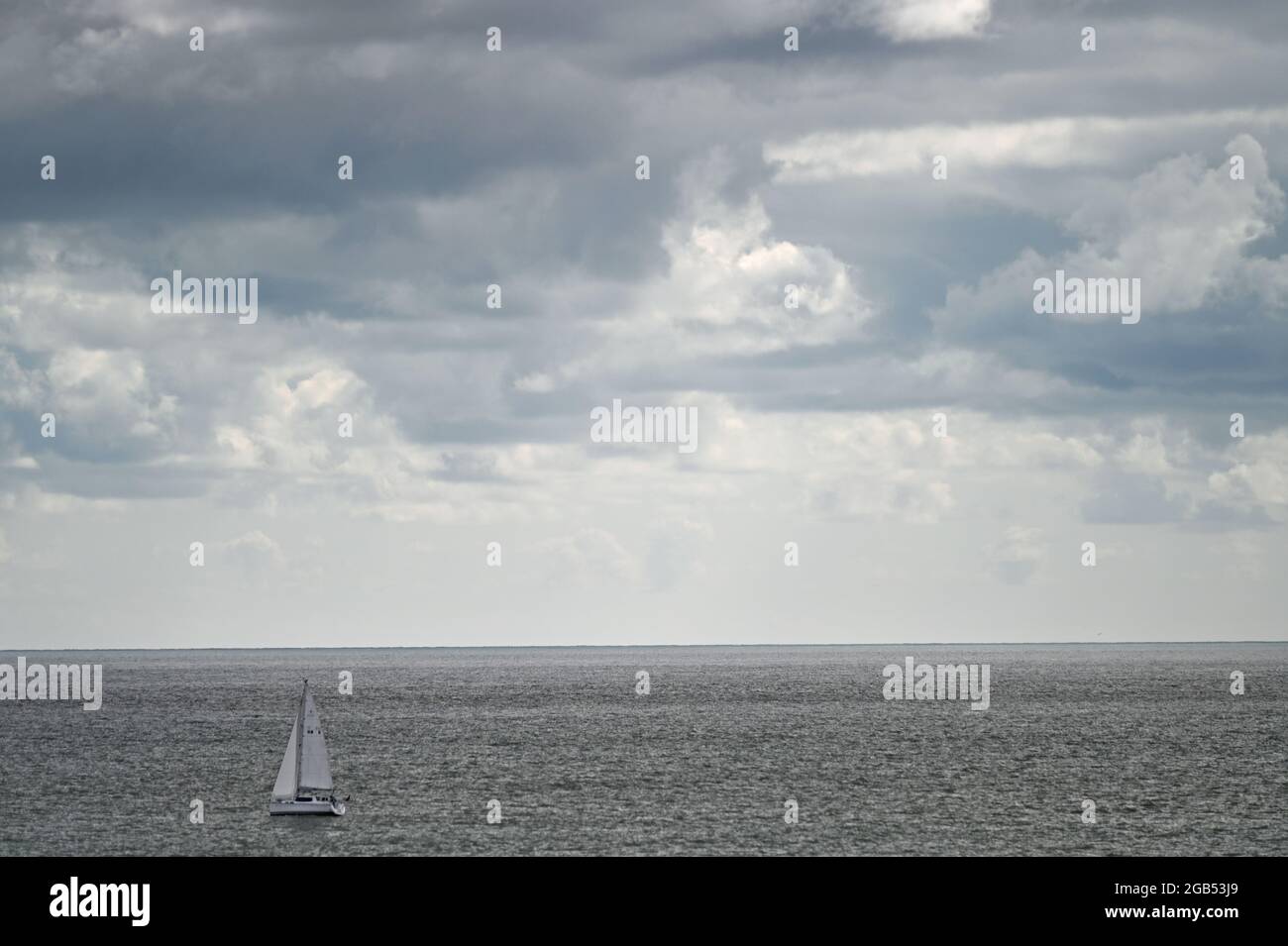 A single sail boat on the North Sea off the coast of Lowestoft, Suffolk, with storm clouds gathering about the sails Stock Photo