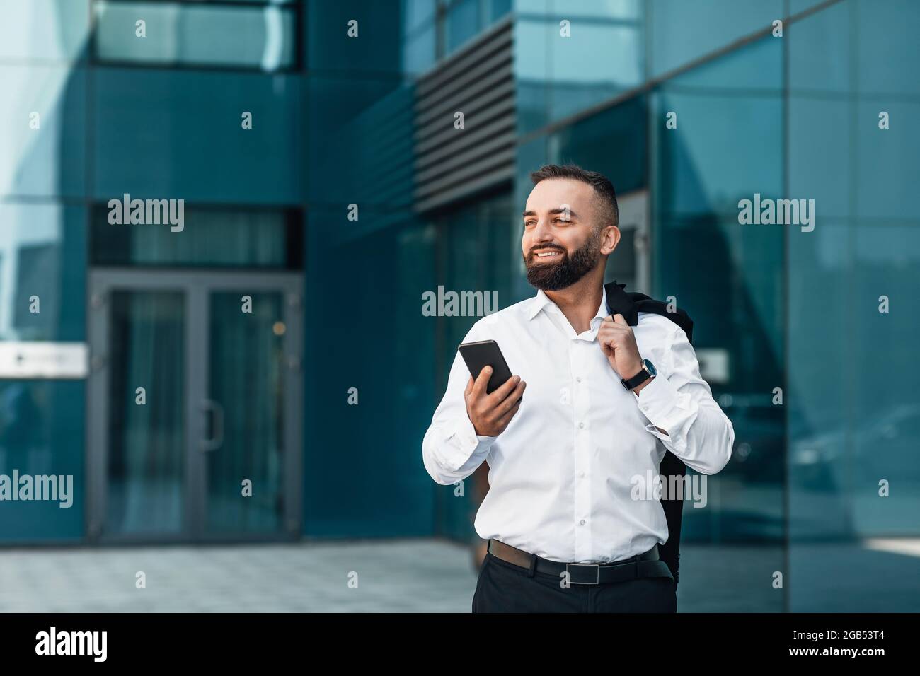 Handsome mature businessman browsing net on cellphone during coffee break, walking near office, copy space Stock Photo