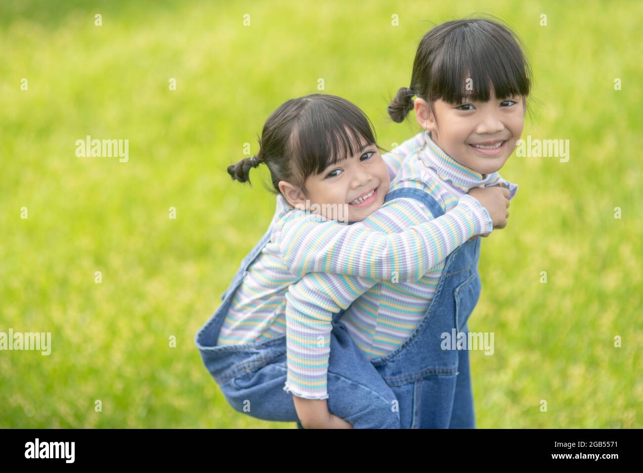 Asian Little girl with elder sister at a park riding on her back Stock Photo