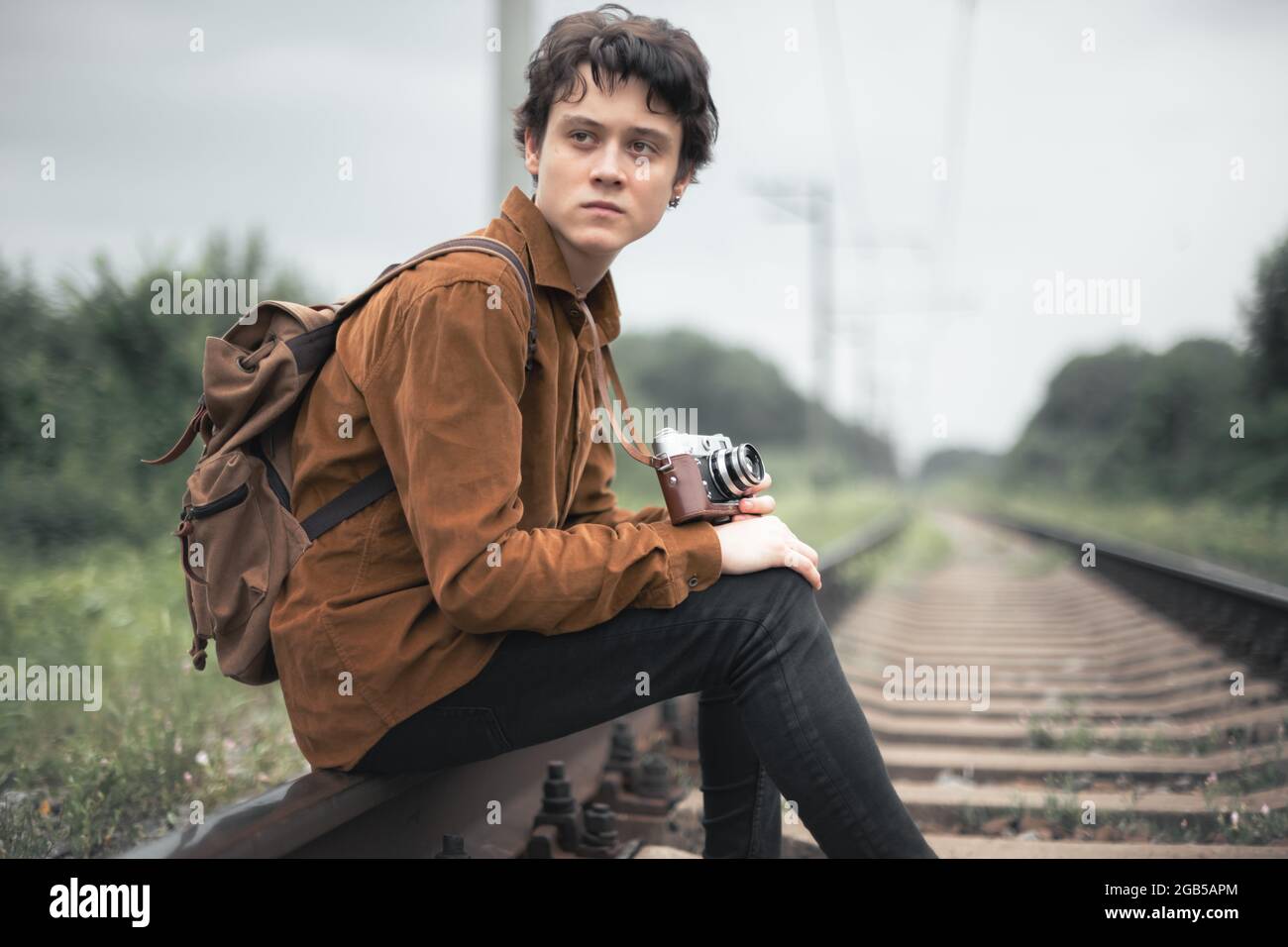 Photographer in brown jacket with backpack and retro camera on railroad Stock Photo