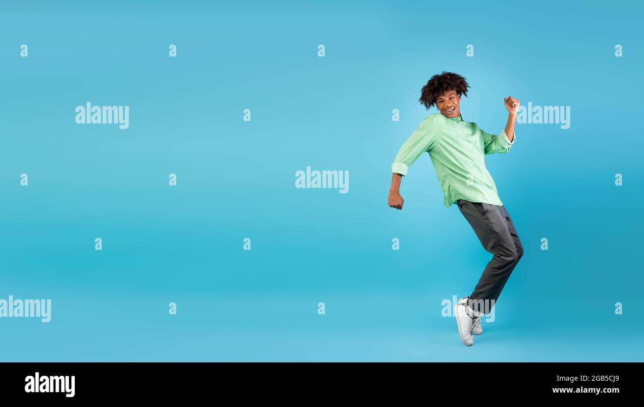 Excited african american teen guy fooling, standing on sneakers tiptoes over blue background, panorama with free space Stock Photo