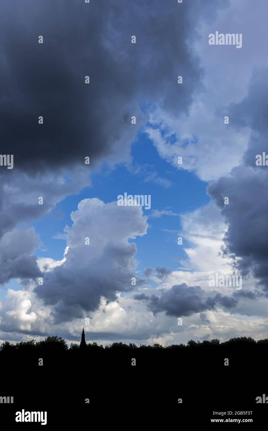 Gap in white and grey cumulus clouds showing patch of blue sky on a rainy day in summer Stock Photo