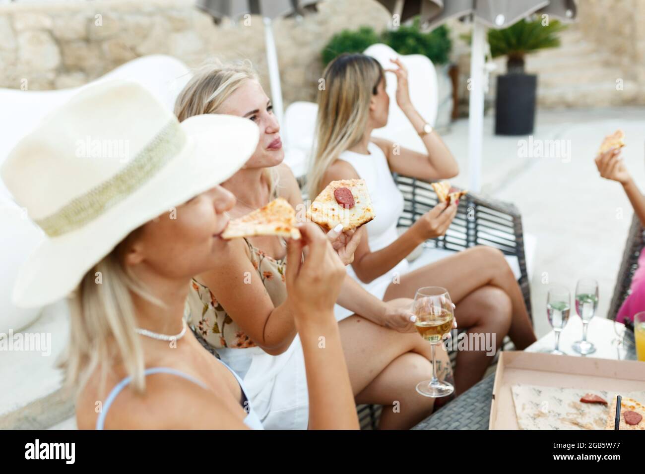 Multiracial friends girls hanging out with drinks,eating pizza together, diverse millennial people sharing pub cafe pizzeria table, smiling students c Stock Photo