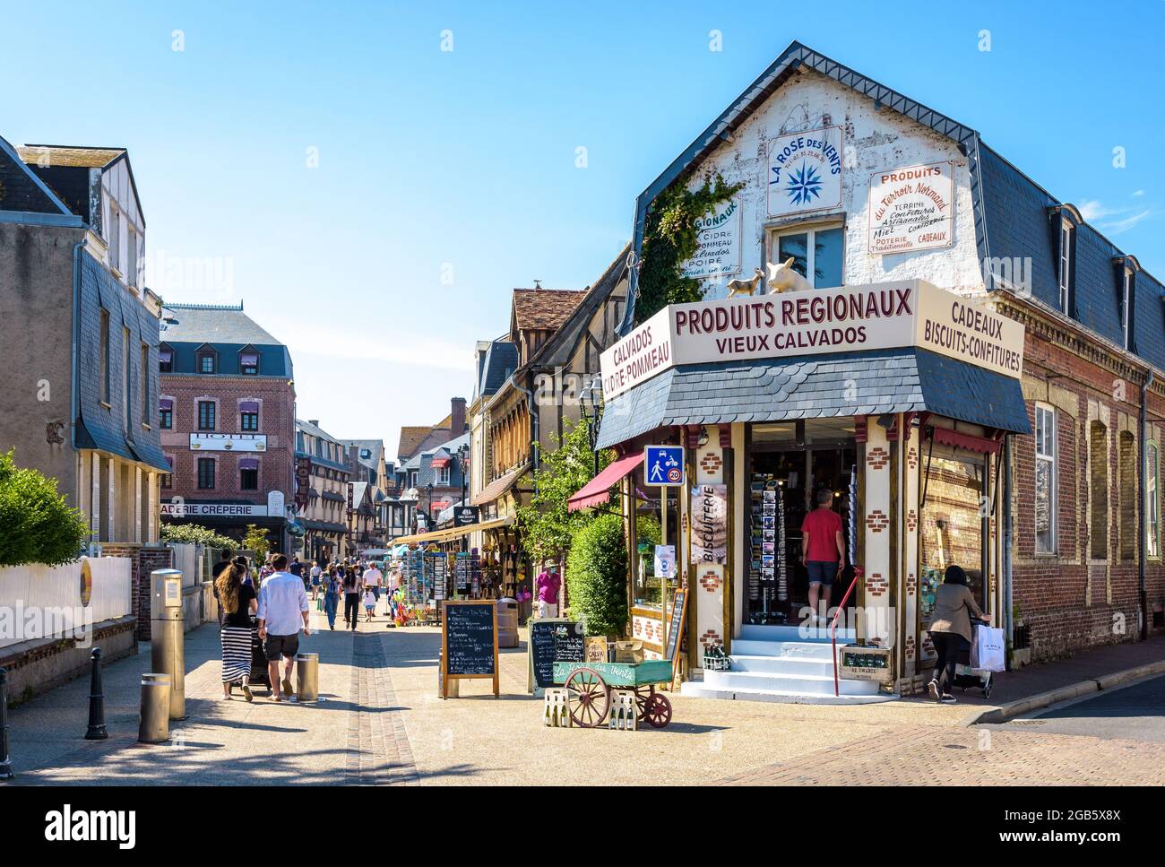 Tourists are strolling in the Monge street in Etretat, France, lined with typical buildings, sidewalk cafes and gift shops on a sunny day. Stock Photo