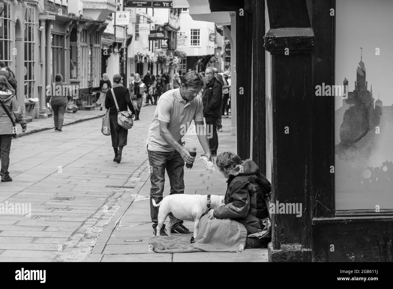 A homeless person sat on a city street receiving a food and beverage donation from a friendly bystander, York, North Yorkshire, England, United Kingdom. Stock Photo