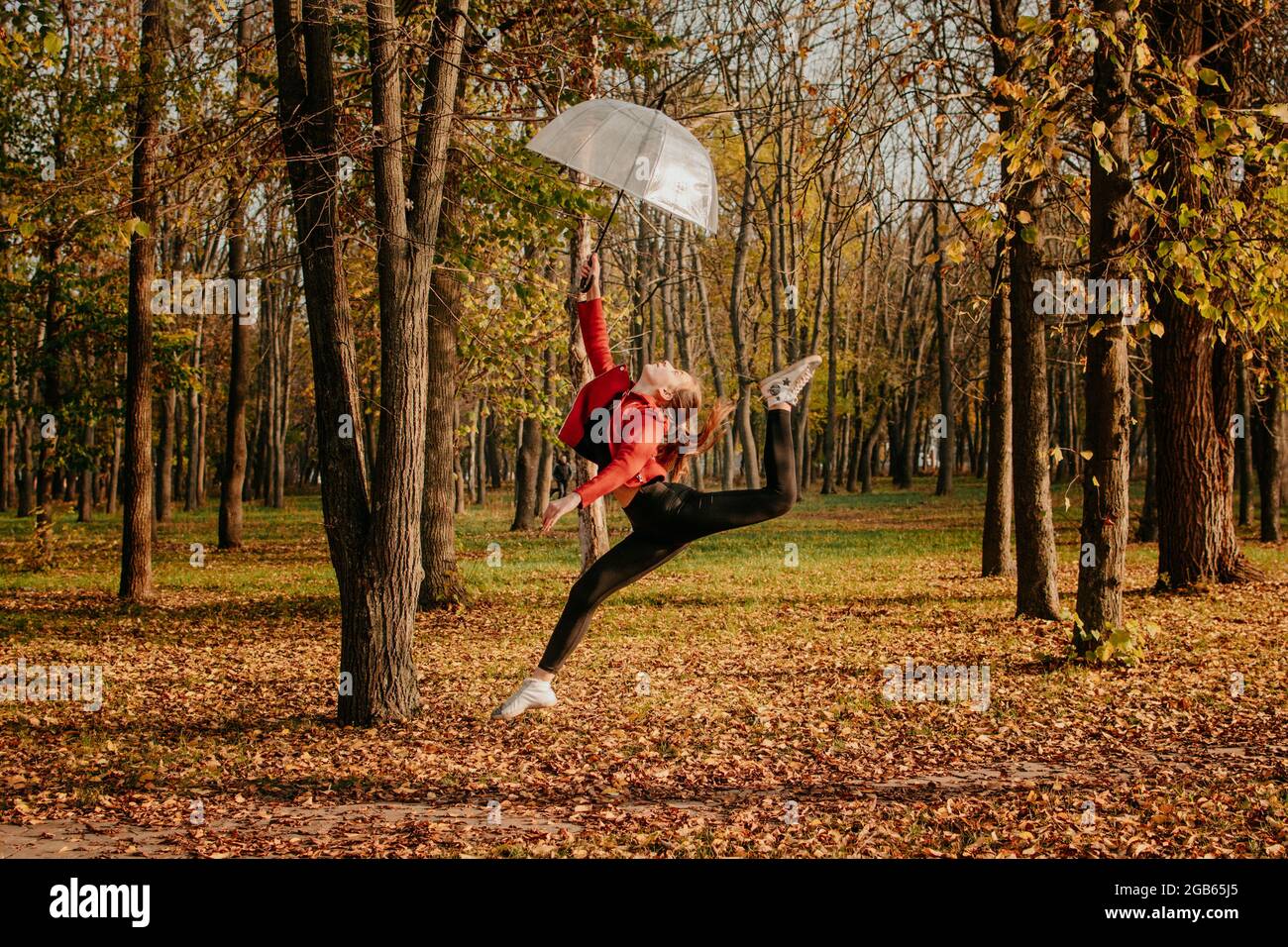Hello fall, autumn season, fall mood, positive emotions. Teenager girl jumping with transparent umbrella and enjoying life in autumn sunny park Stock Photo