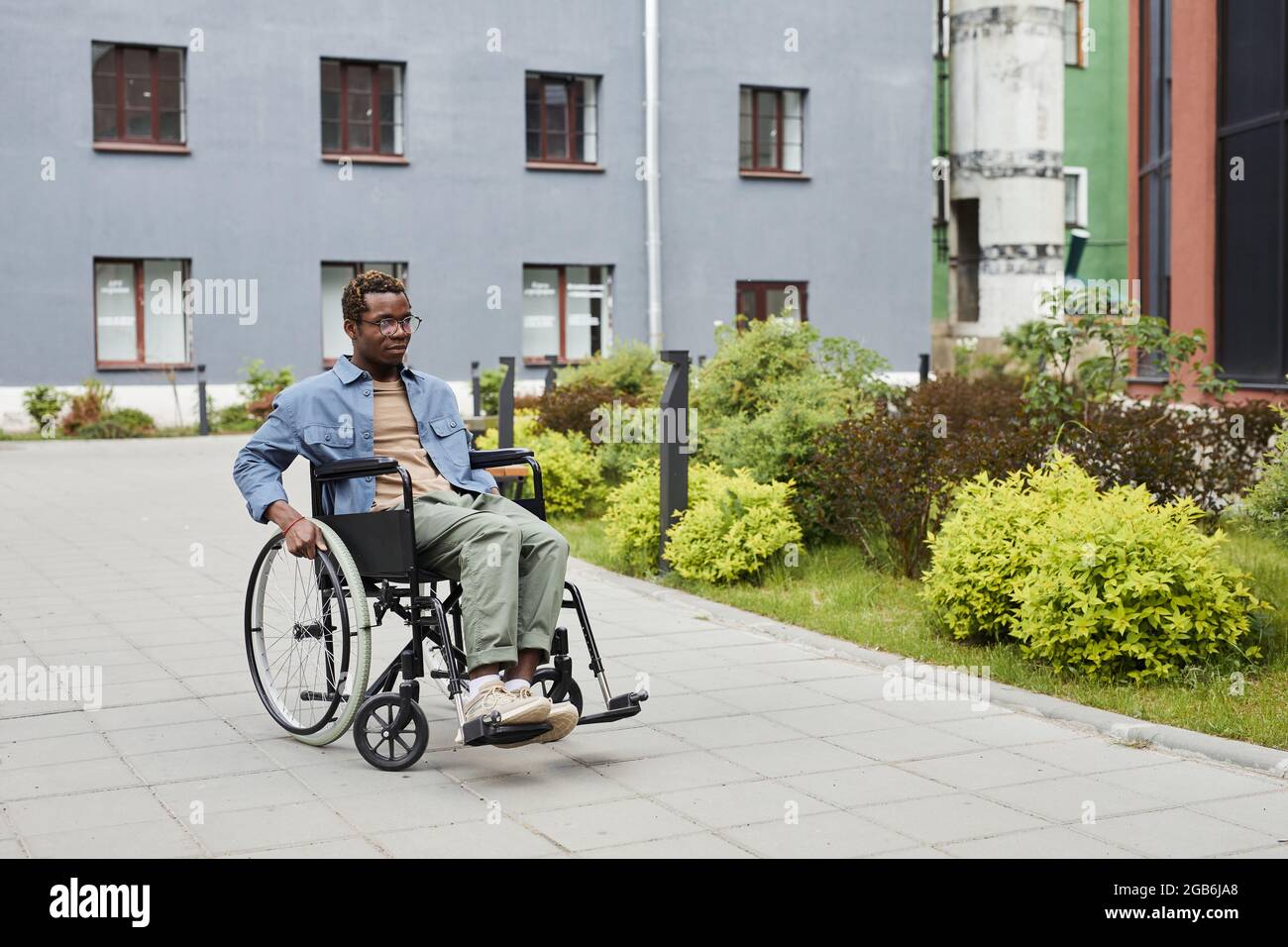 Serious handicapped young African-American man in eyeglasses sitting in wheelchair outdoors Stock Photo