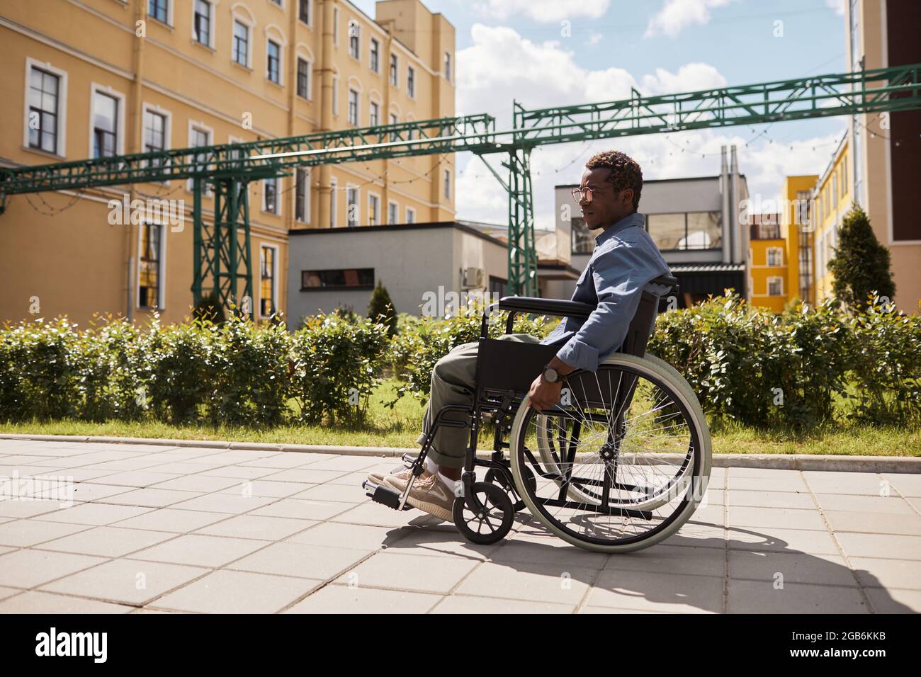 Sad pensive young black disabled man in glasses using wheelchair while walking down street alone Stock Photo