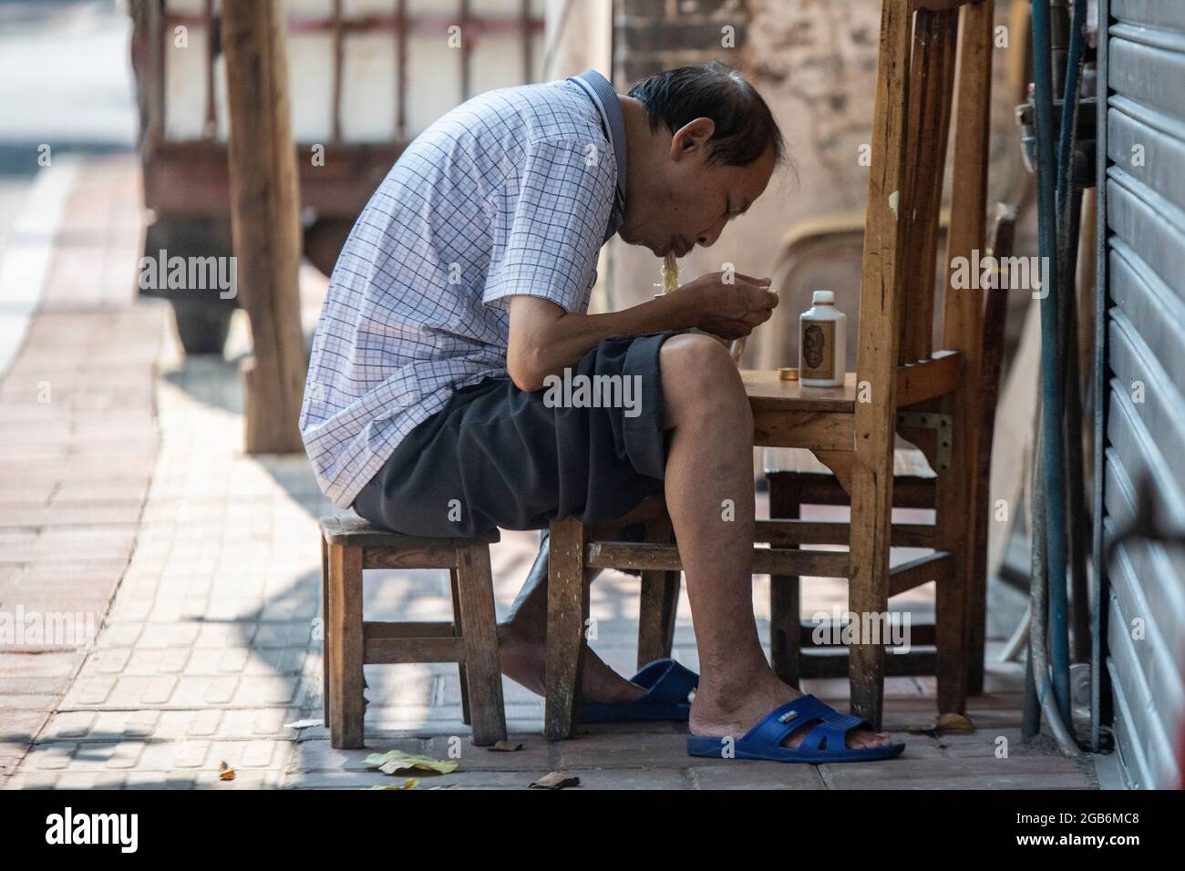 A man reats his noodles outside on a makeshift table in a village in China Stock Photo