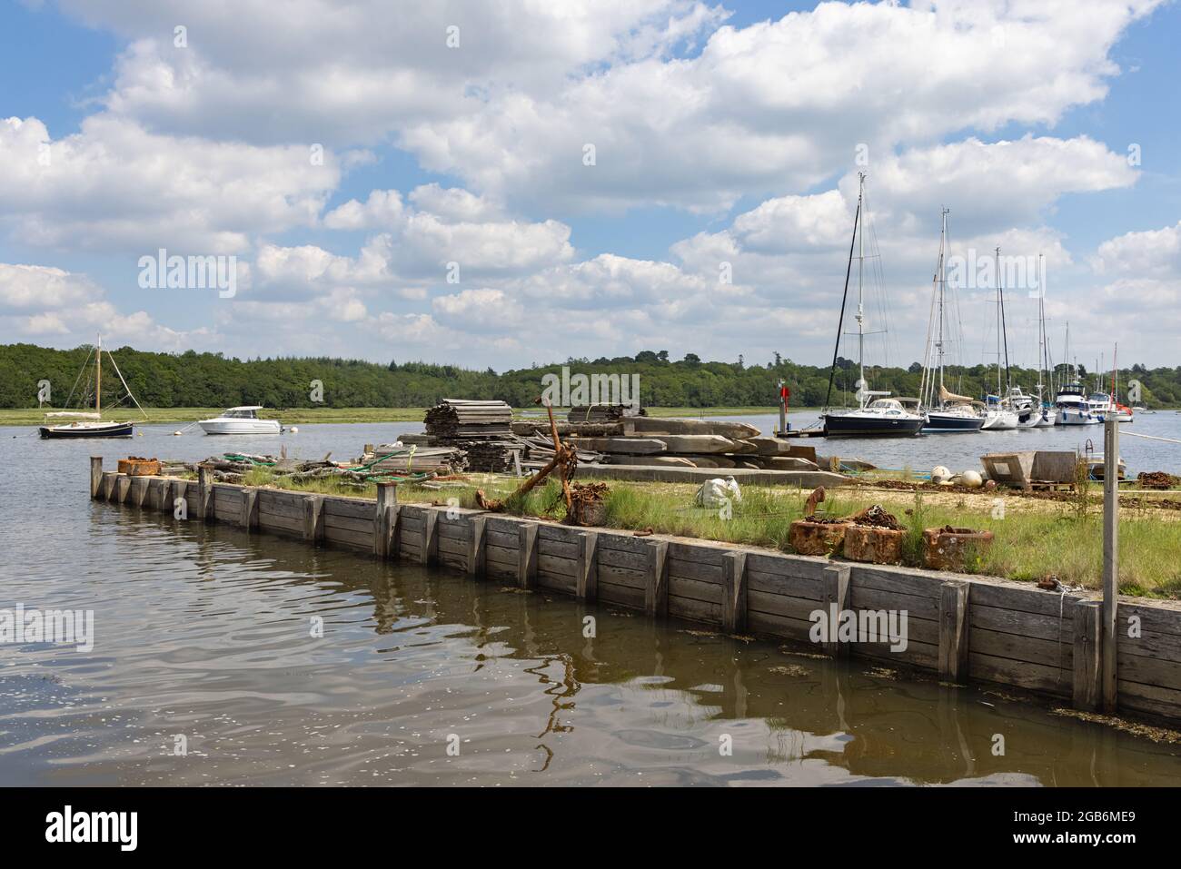 Buckler's Hard, Hampshire, UK, June 23rd 2021: A rusty anchor and chains on a wooden quayside juts into the Beaulieu River on which yachts are moored. Stock Photo