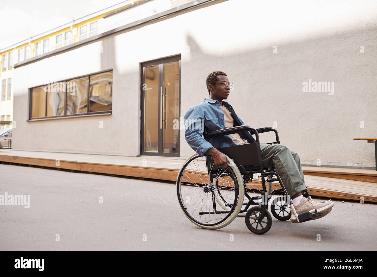 Serious handicapped young African-American man in eyeglasses using wheelchair while walking alone Stock Photo