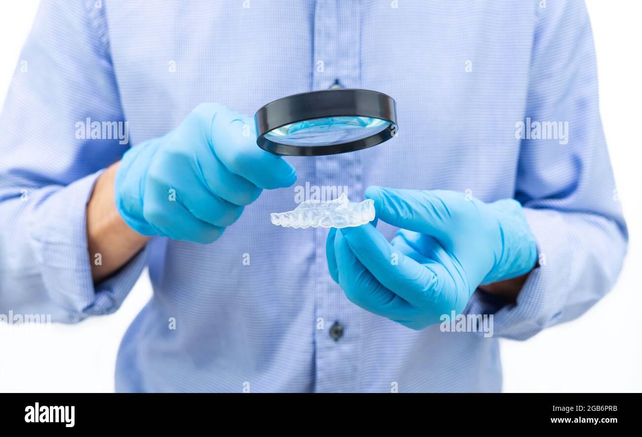 Dentist in blue gloves and shirt examining a clear dental splint with ...