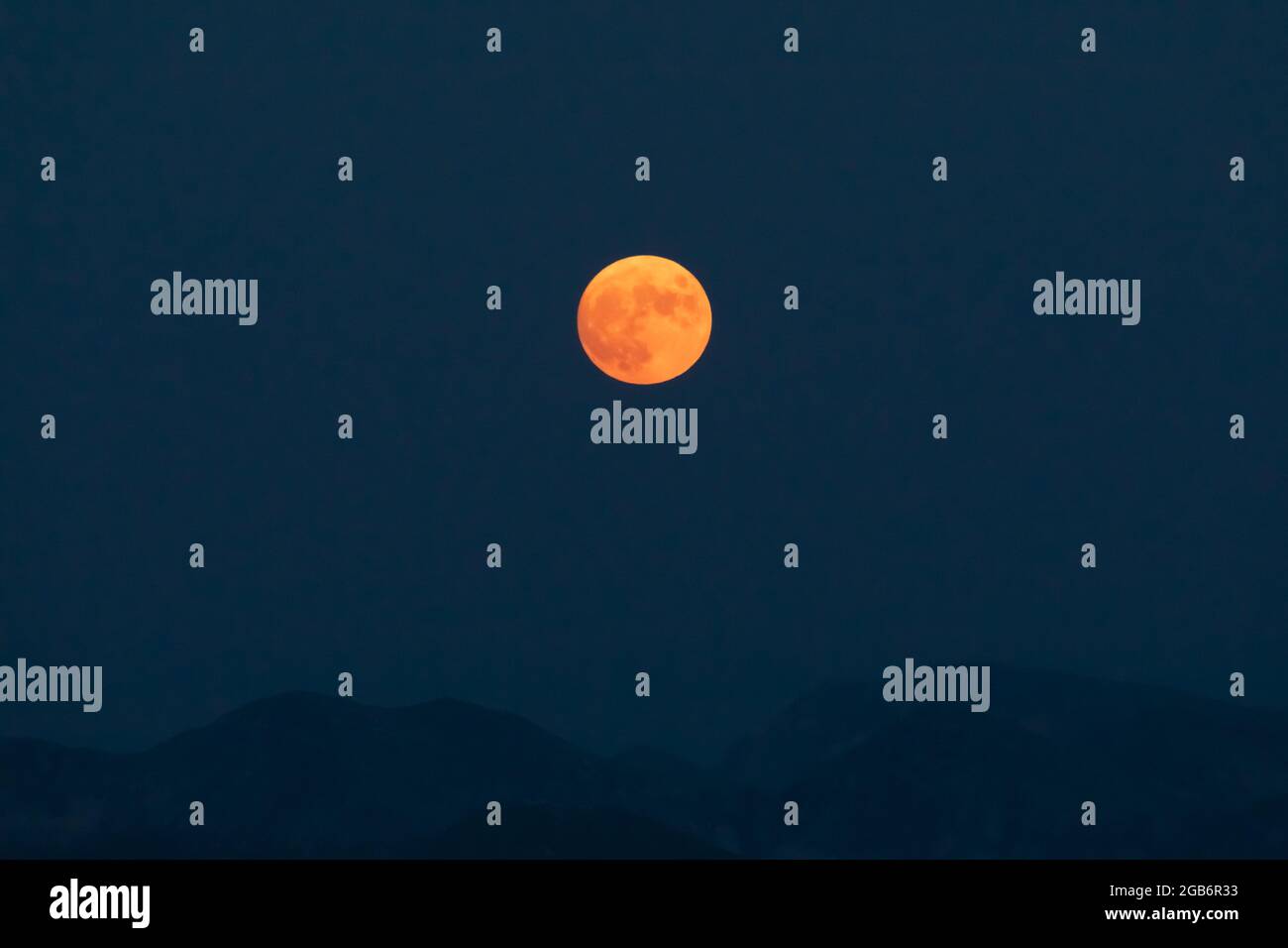 Splendid full red moon rises over the mountain ridges of the Apennines ...