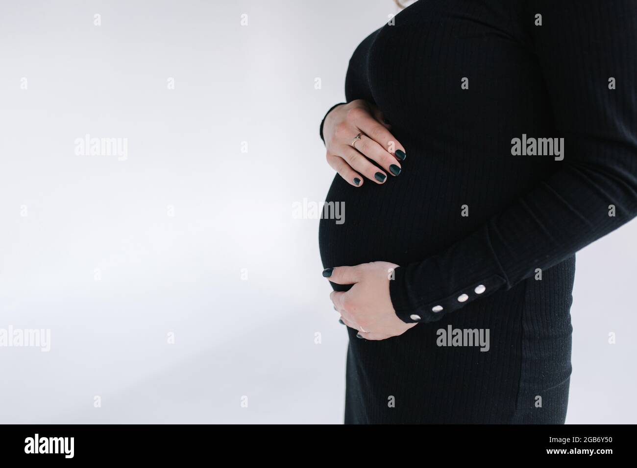 Middle selection on pregnant woman puts hands on her belly. Female in black bodycon dress. White background Stock Photo