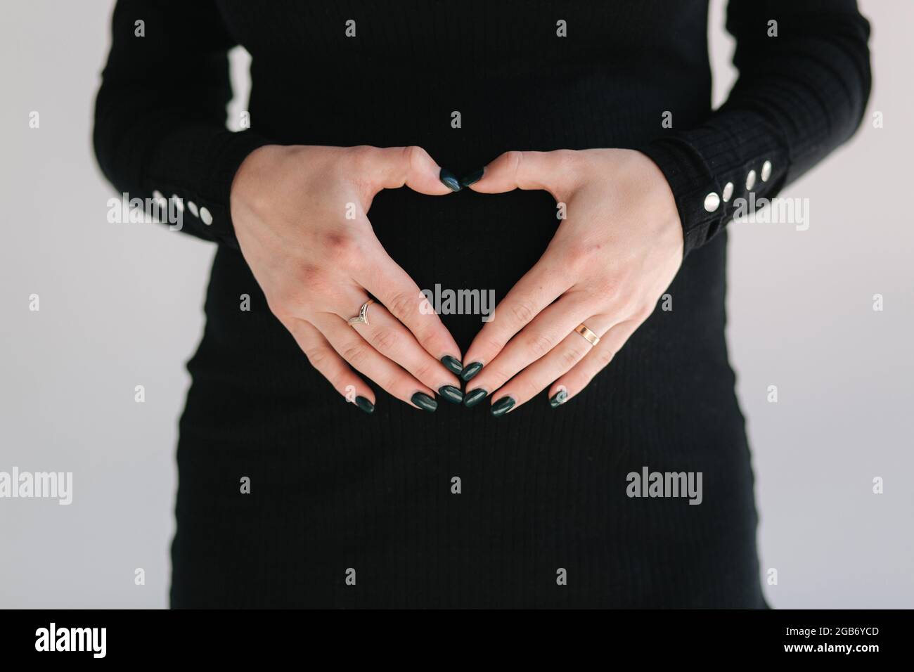 Middle selection on pregnant woman puts hands on her belly. Female in black bodycon dress. White background Stock Photo