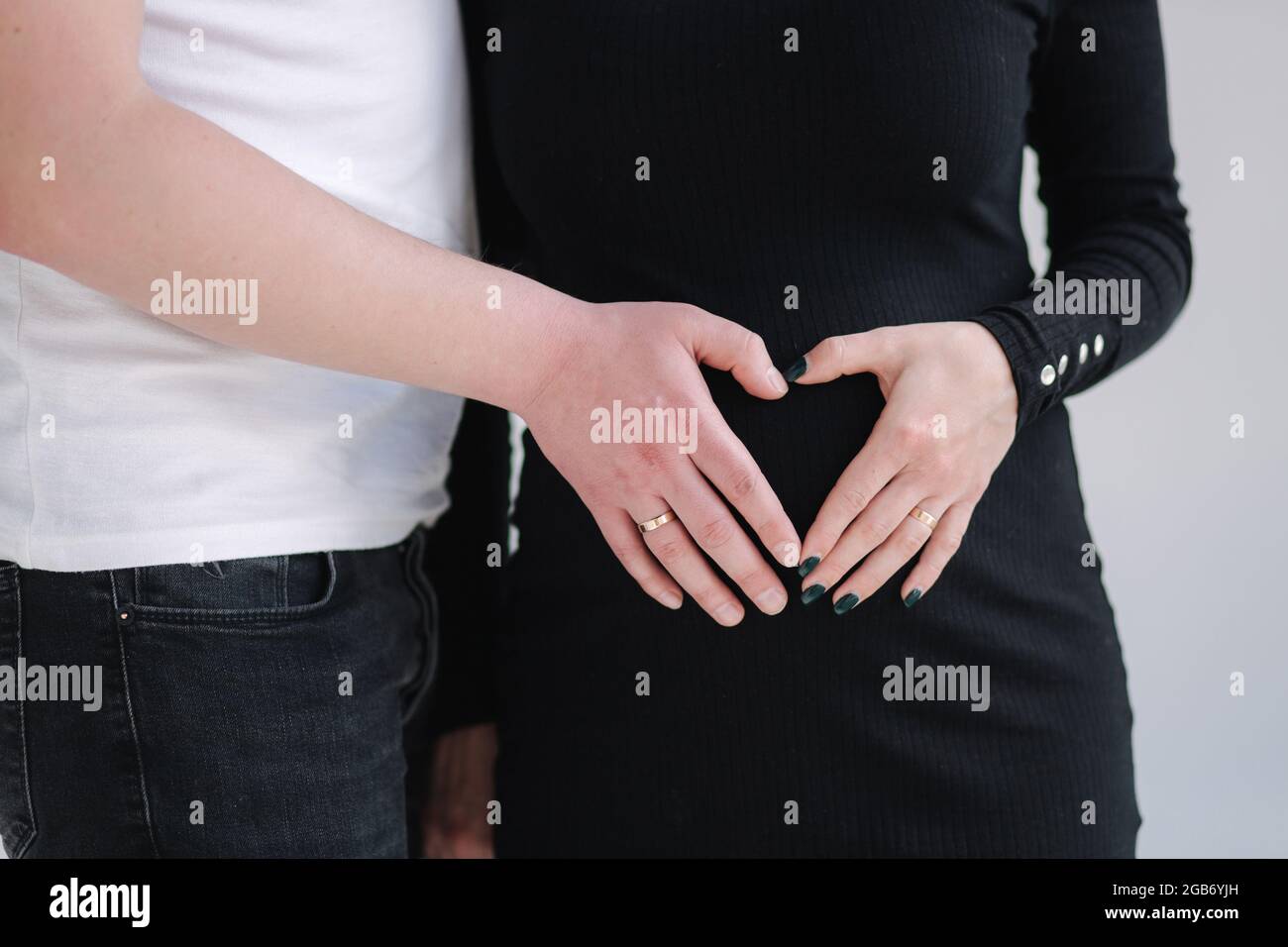 Middle selection on pregnant woman with her lovely husband puts their hands on her belly. Female in black bodycon dress. White background Stock Photo