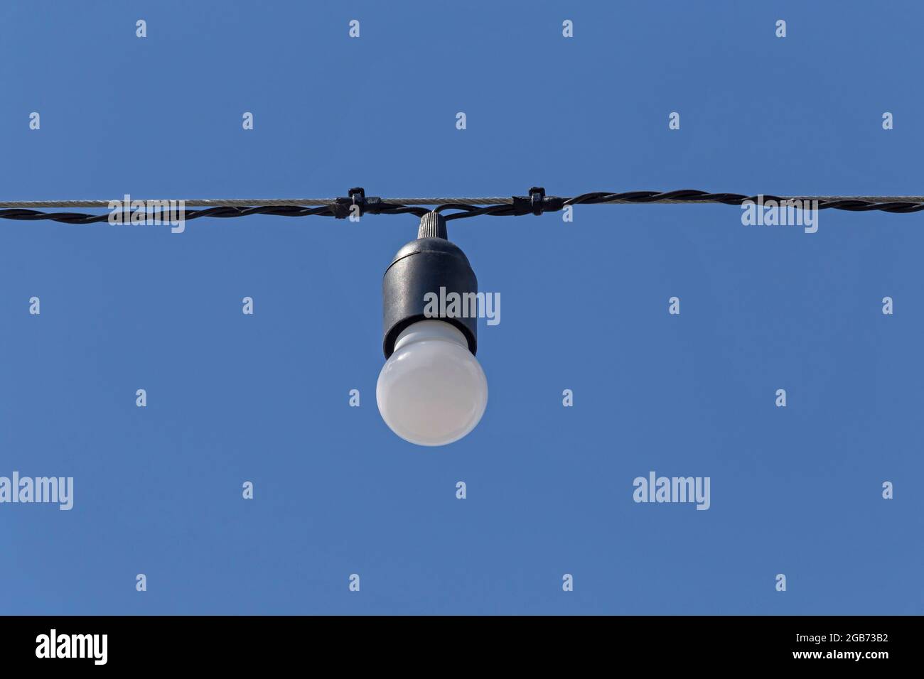 electrical bulb hanging on cable against blue sky Stock Photo