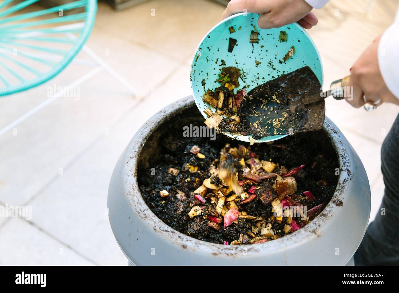 Woman doing compost in the backyard of his house. She is throwing waste of vegetables in the composter. Stock Photo