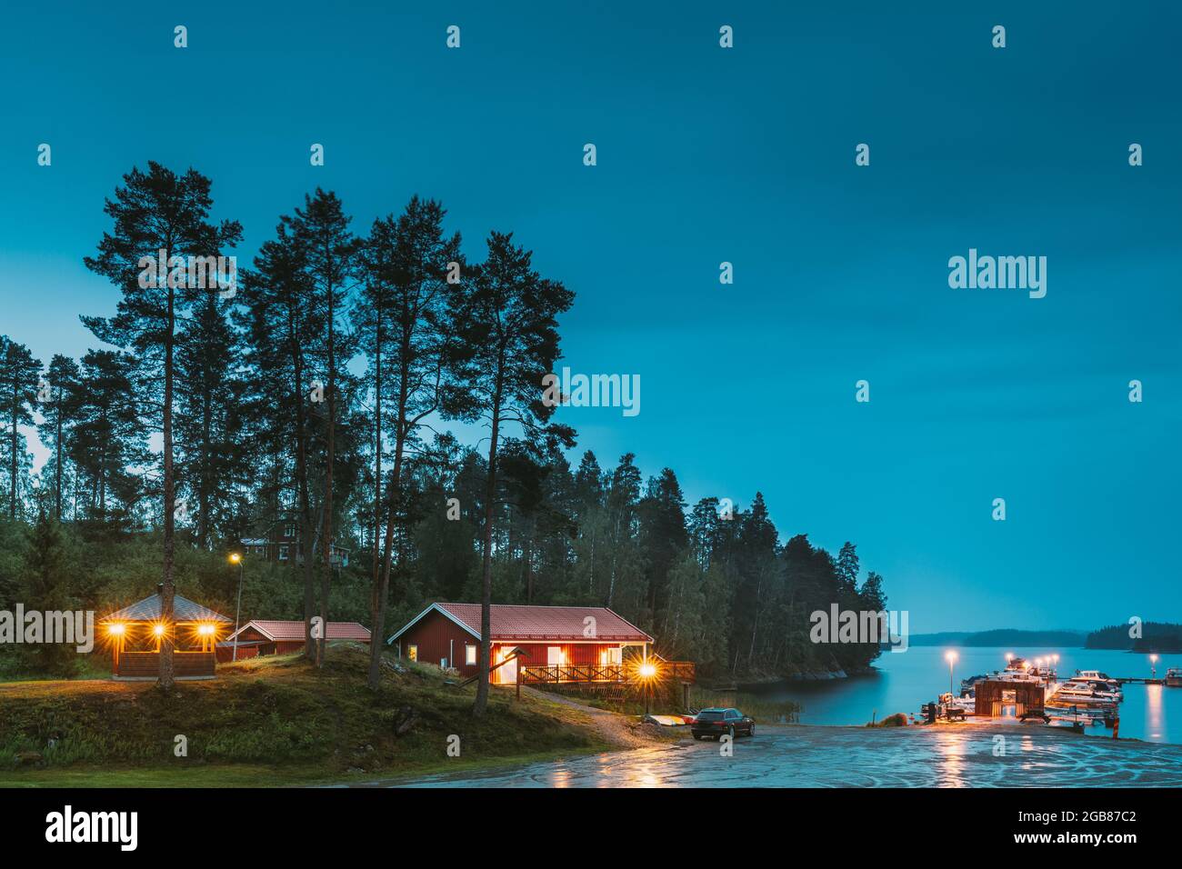 Sweden. Sweden. Beautiful Red Swedish Wooden Log Cabin House On Rocky Island Coast In Summer Night Evening. Lake Or River Landscape. Beautiful Wooden Stock Photo
