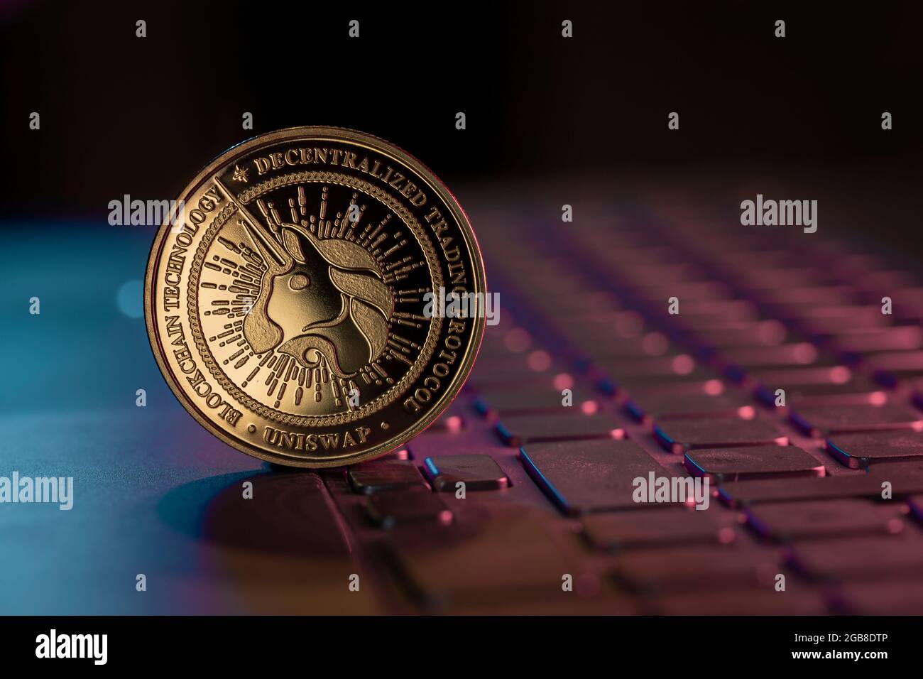Uniswap UNI cryptocurrency physical coin placed on laptop keyboard and lit with aqua and purple lights Stock Photo