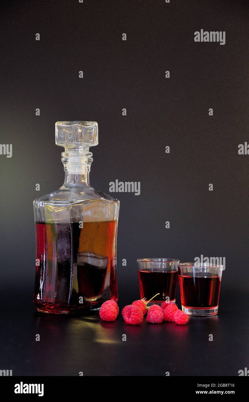 Homemade raspberry liqueur in two glasses and a bottle, ripe berries ...