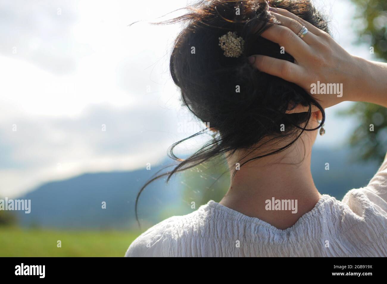 A girl is holding her hair. The little flower in the hairstyle. Natural ethnic style in the mountains. Stock Photo
