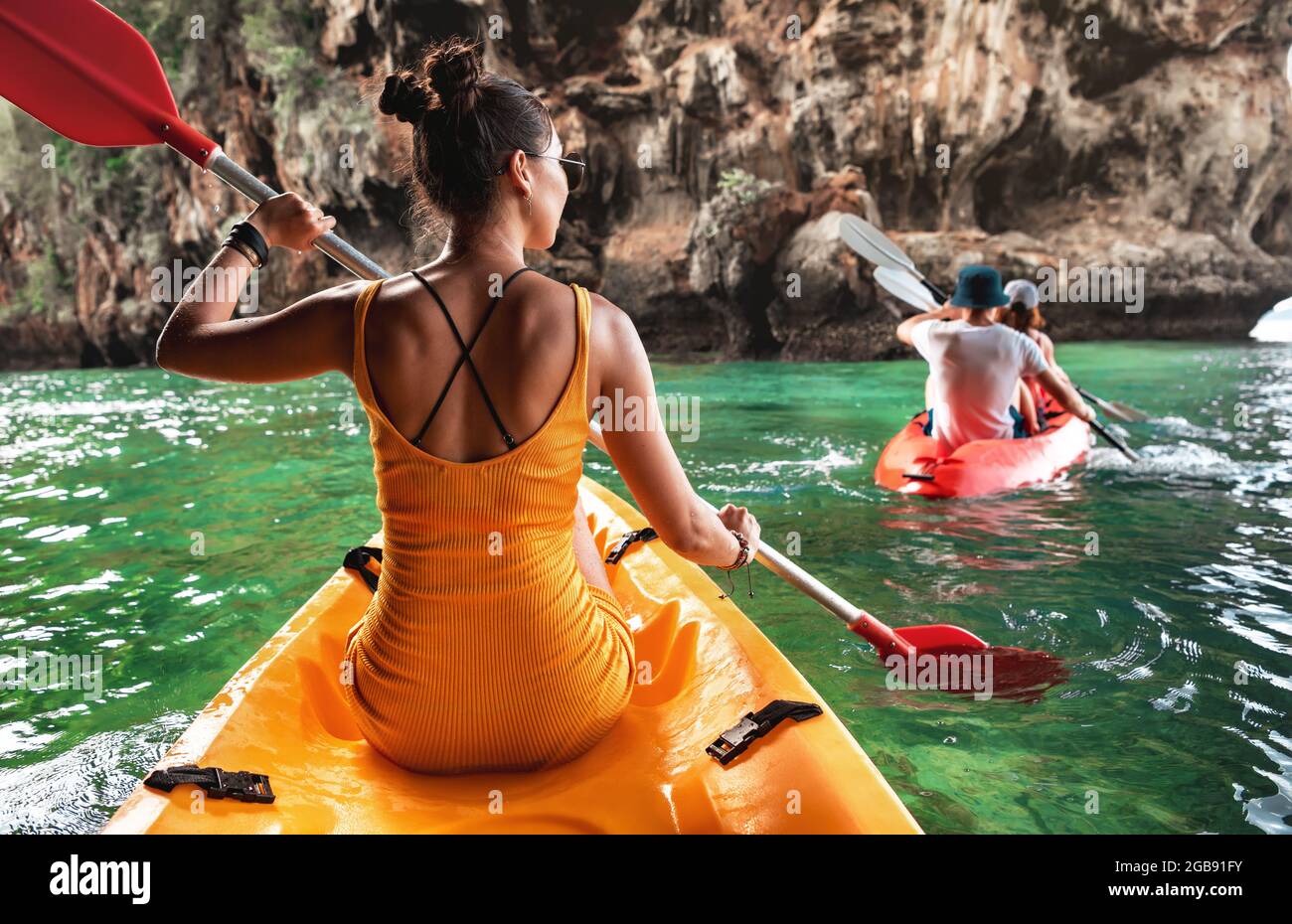 Beautiful sporty young girl with friends walks on a yellow kayak along a picturesque tropical bay. Phranang Railay beach, Krabi province, Thailand. Stock Photo