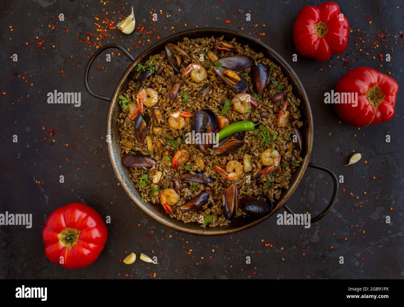 Black paella with seafood and squid ink with tomatoes on a black