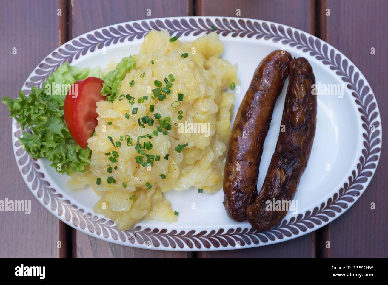 Two Nuremberg bratwursts with potato salad on an oval plate in a garden restaurant, Bavaria, Germany Stock Photo