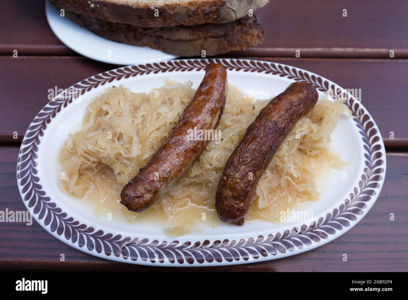 Two Nuremberg bratwursts with sauerkraut and bread on an oval plate in a garden restaurant, Bavaria, Germany Stock Photo