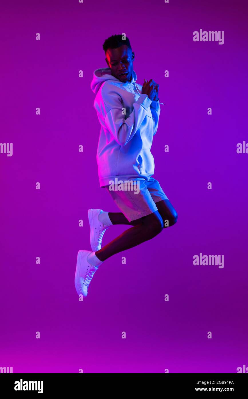 Full lenght portrait of young energetic African American man jumping in dark purple futuristic cyberpunk neon light background Stock Photo