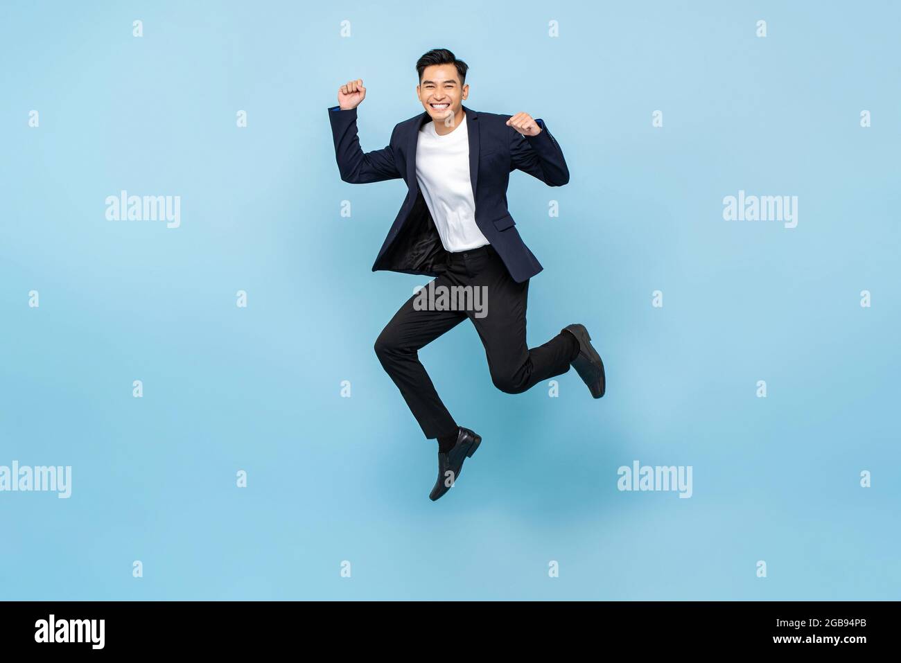 Full lenght portrait of ecstatic handsome Asian man jumping and raising  his fists on isolated light blue studio background Stock Photo