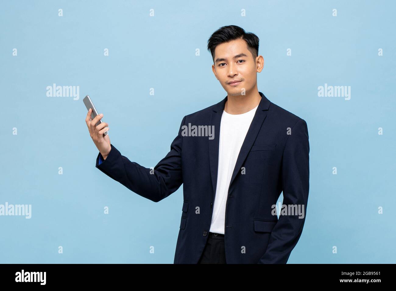 Young handsome Asian man in semi formal suit holding mobile phone and ...