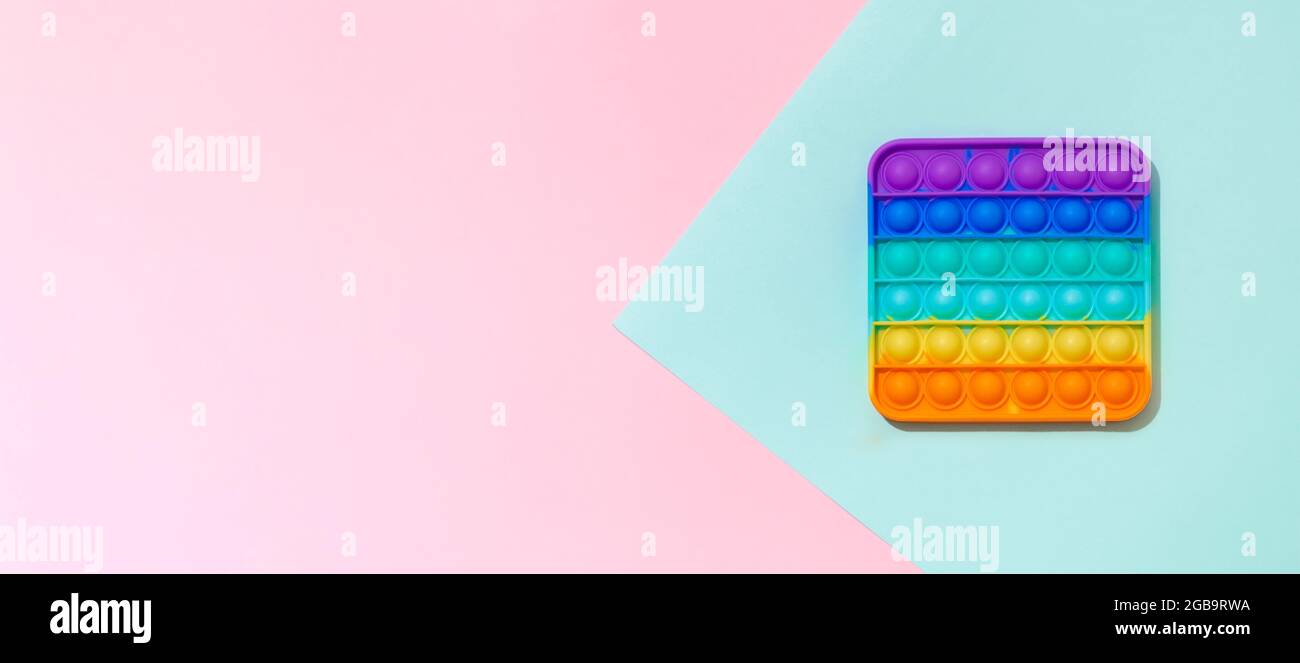 Popit on blue and pink background with copy space. Popular silicone colorful antistress pop it toy for child. Top view from above. Simple dimple. Horizontal banner Stock Photo