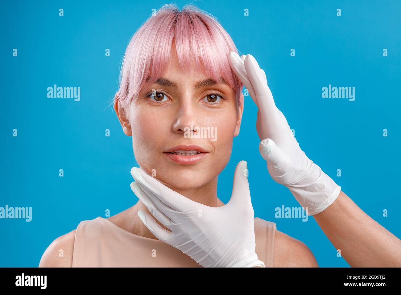 Hands of beautician examining female face before giving facial botox injections isolated over blue background Stock Photo